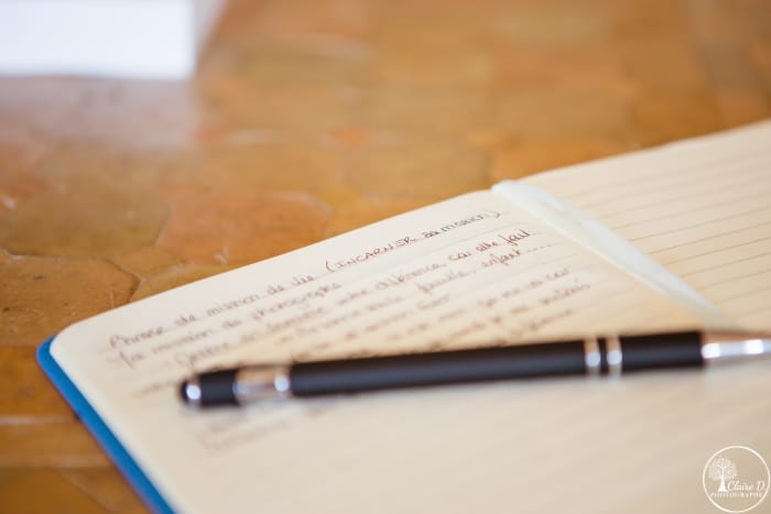 cahier ouvert avec un stylo posé dessus sur un carrelage marron