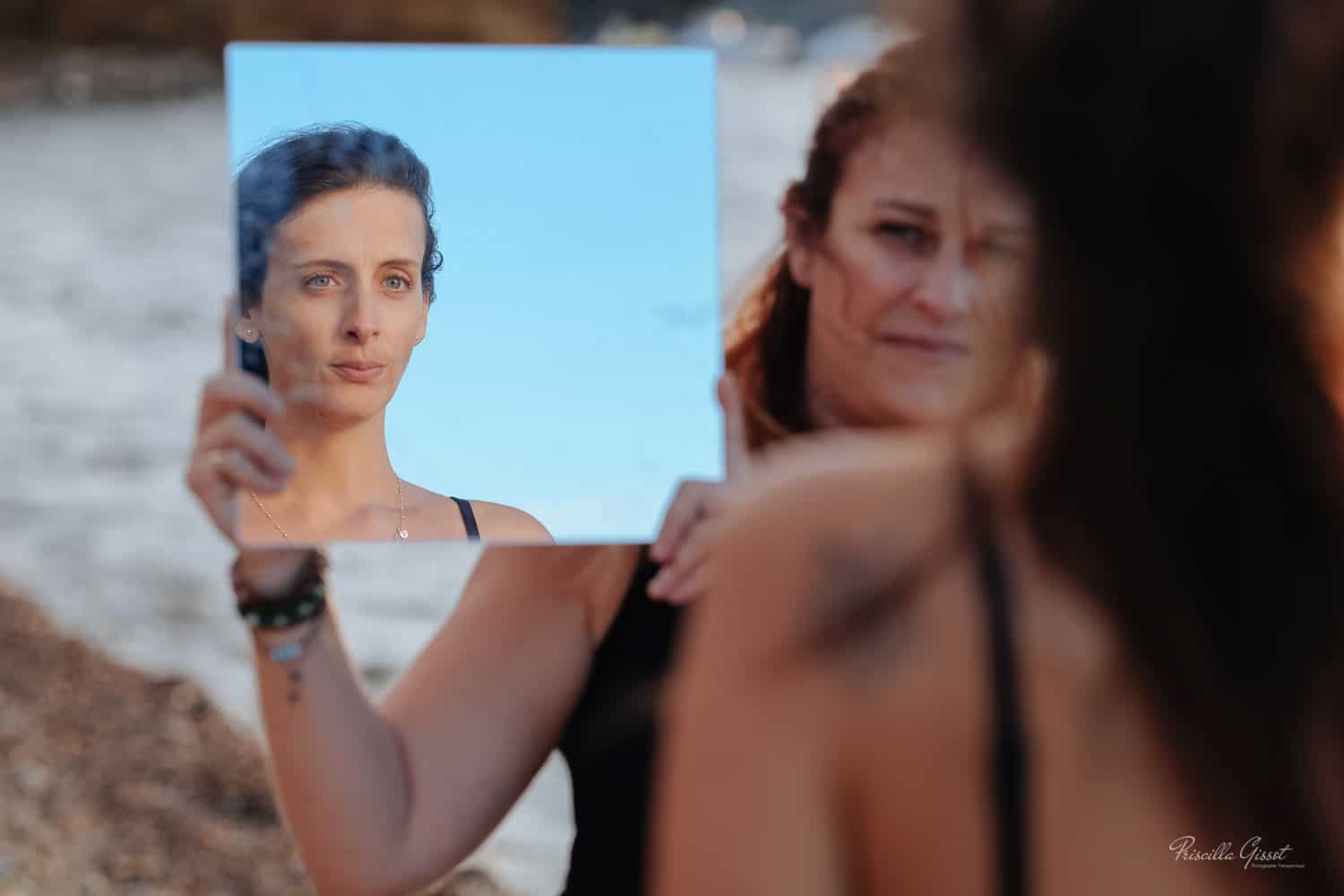 une femme qui se regarde dans un miroir tenue par une autre en face d'elle