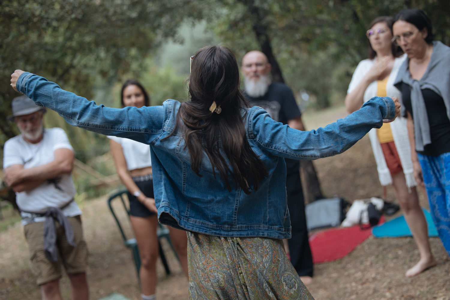 Une femme les bras ouverts dans la nature, partageant un moment de libération et de vulnérabilité lors d’une retraite holistique axée sur la connexion à soi et aux autres.