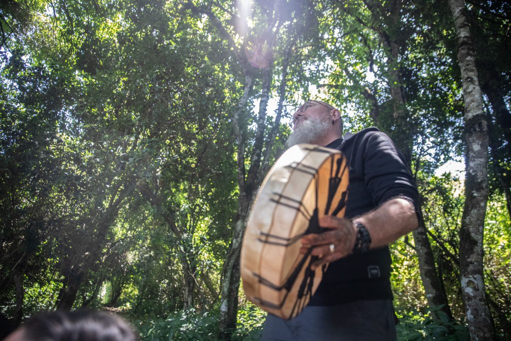 Homme participant à une retraite spirituelle pour hommes, jouant du tambour en pleine nature, symbole du développement personnel chez l'homme.