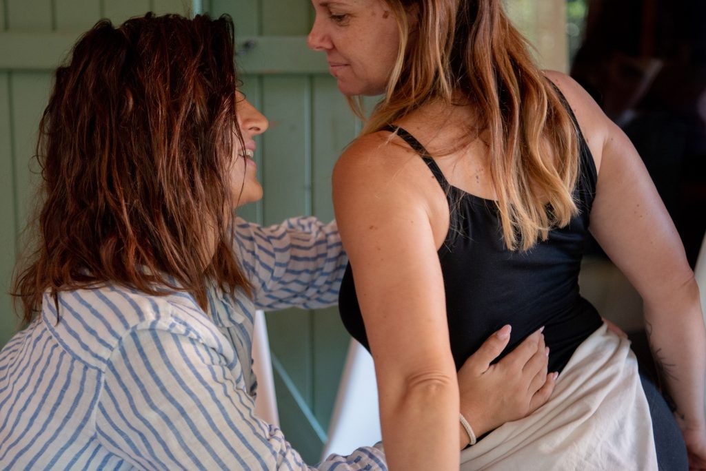 Une femme accompagne une autre avec bienveillance dans un exercice de connexion corporelle, symbolisant l’évolution des relations et l’acceptation du changement.