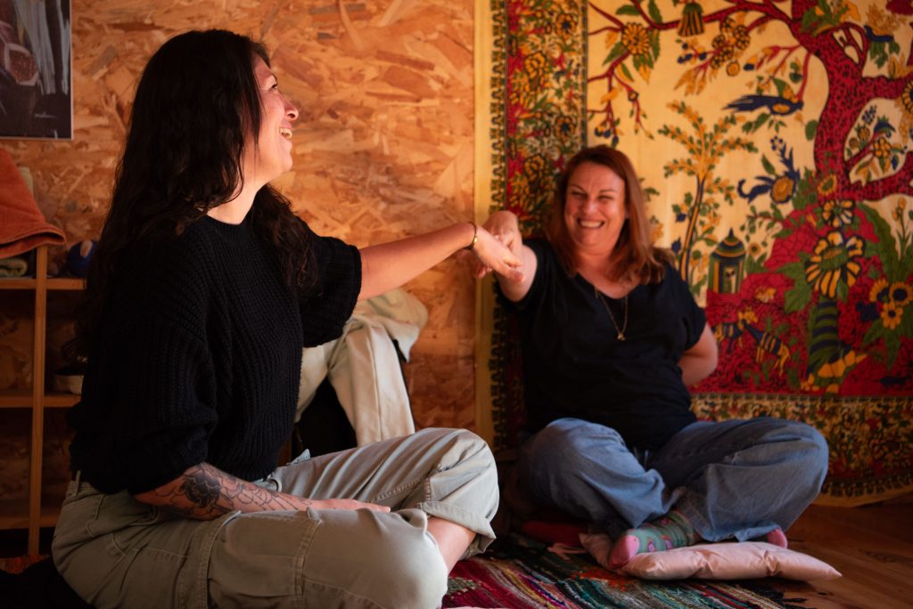  Deux femmes échangent un regard complice et se tiennent la main lors d'une retraite bien-être, illustrant la profondeur du lien et l'évolution naturelle des relations.
