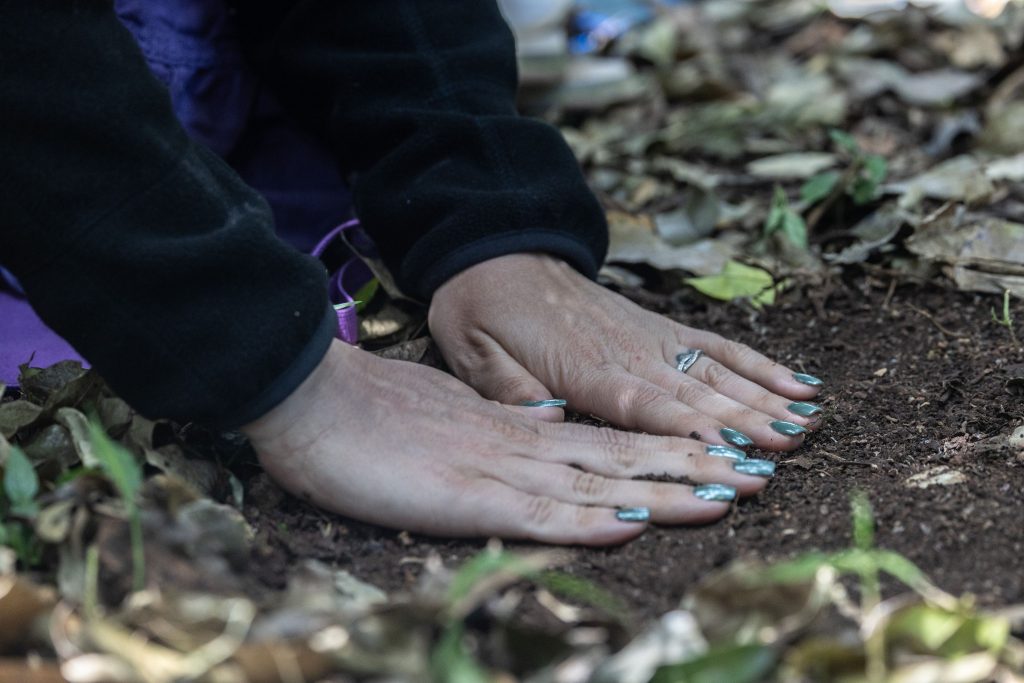  Mains posées sur la terre lors d’un rituel de connexion à la nature pendant la retraite HUMAN, symbolisant l’ancrage et la spiritualité.