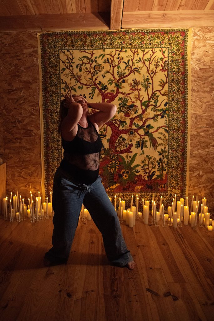 Femme dansant avec intensité devant un mur décoré, entourée de bougies, symbolisant la reconnexion à sa sensualité et son énergie féminine.