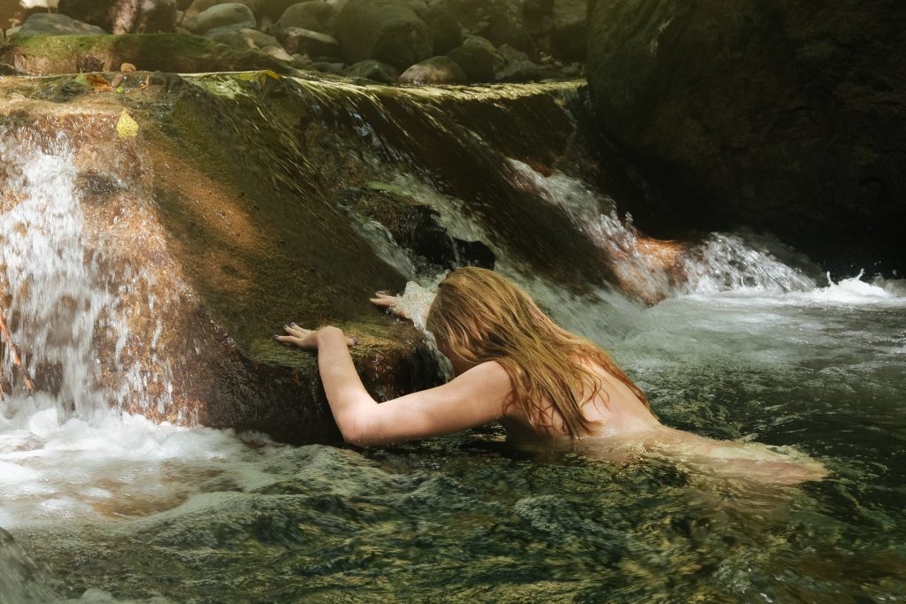 Femme nue en posture de libération et de reconnexion dans l’eau vive d’un torrent guadeloupéen