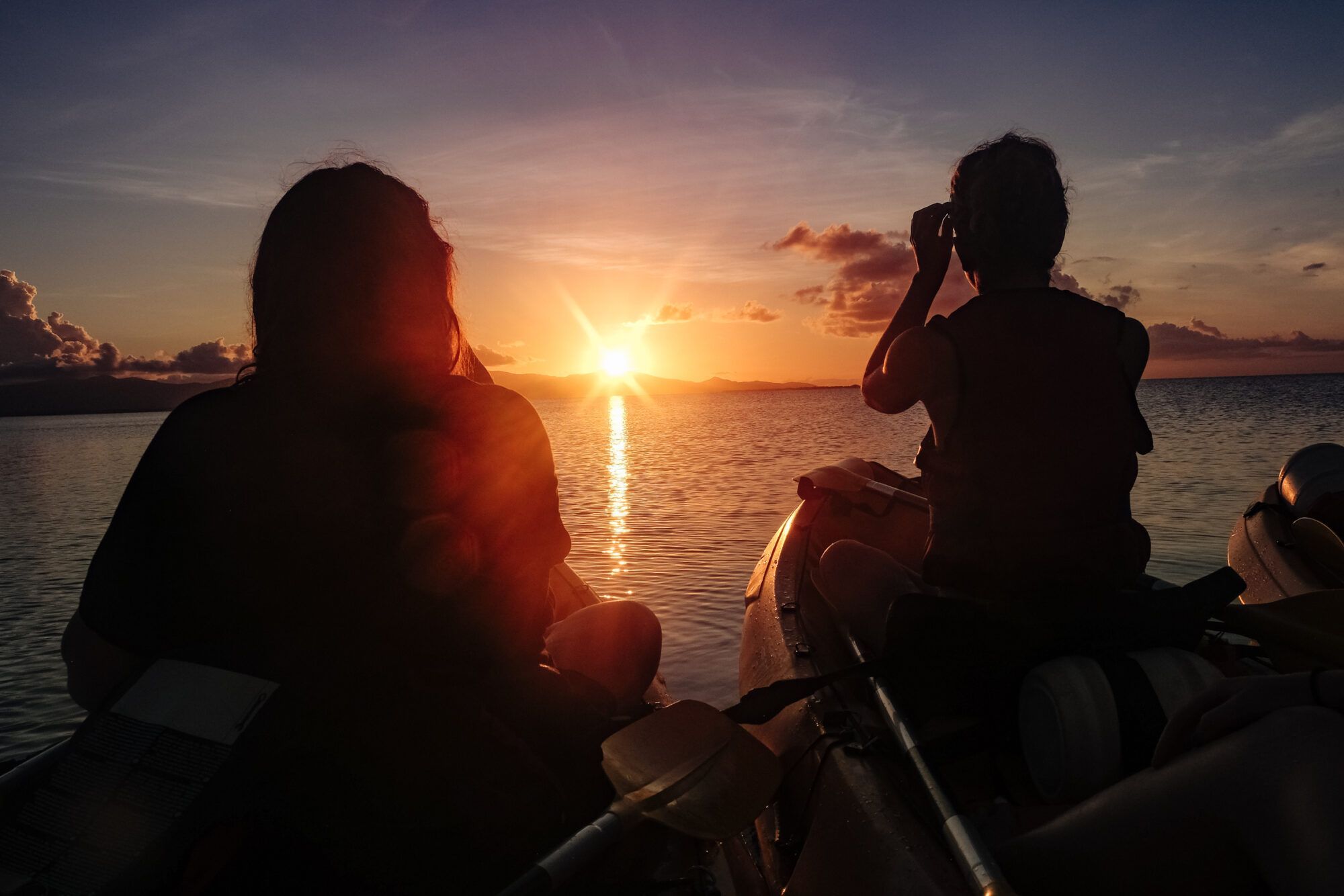 Silhouettes en kayak face au coucher de soleil, moment de liberté intérieure et d’émerveillement.