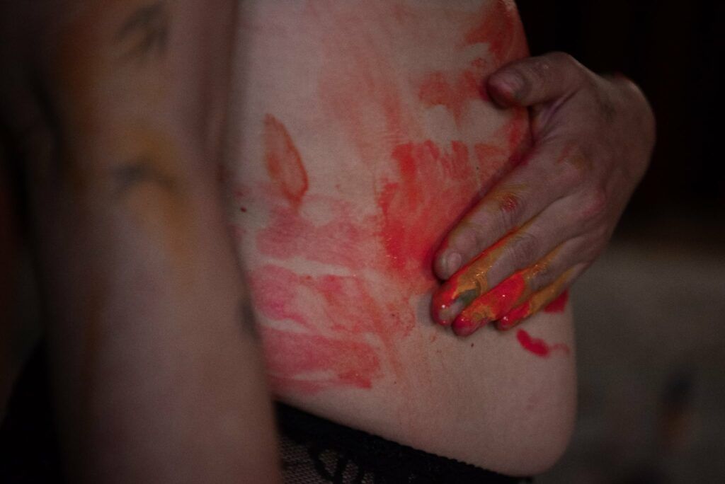 La libido des femmes : quand le désir change de camp dans le couple 1 Main de femme posée sur le ventre, recouvert de peinture rouge et orange, symbole de reconnexion au corps et à la sensualité féminine.