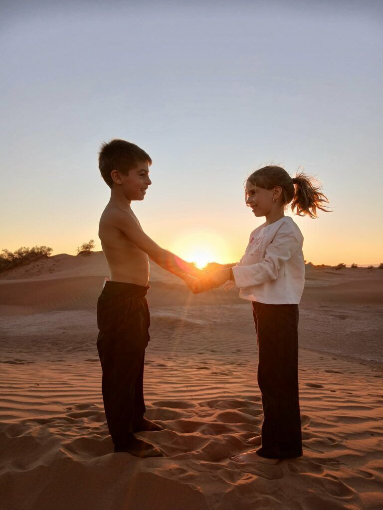 Maman solo entrepreneur : le parcours inspirant de Johanna, fondatrice de Baby Événement 2 Deux enfants se tenant les mains dans le désert au coucher du soleil, symbole du lien fraternel et de la force familiale d’une maman solo entrepreneur.