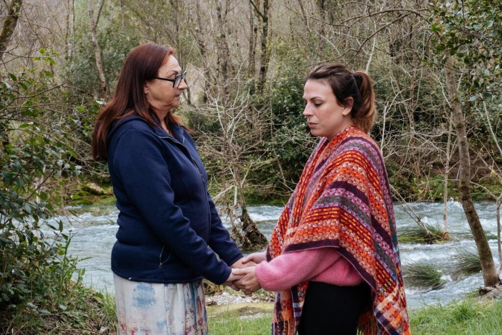 Mère et fille se tenant les mains au bord d’une rivière lors d’un atelier émotionnel pendant une retraite famille sur les liens quand la maladie entre dans une famille.