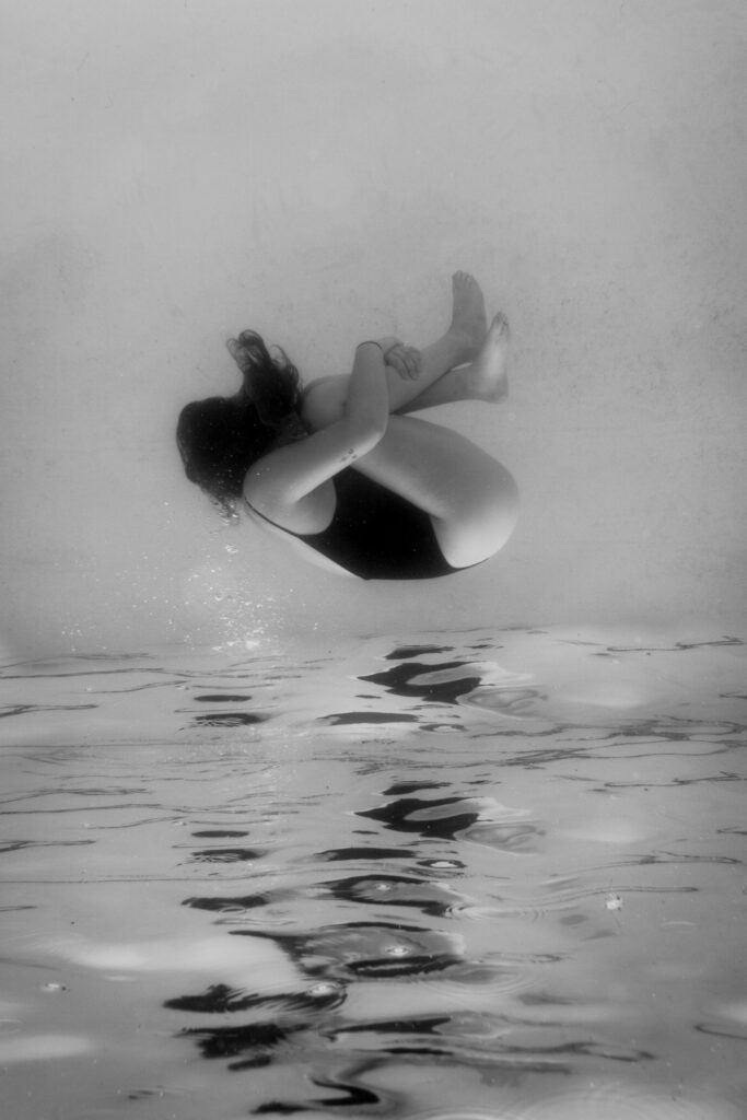 Toujours disponible pour les autres : quand la relation devient à sens unique 1 Femme repliée sur elle-même sous l’eau pendant une séance de photo-thérapie en noir et blanc.