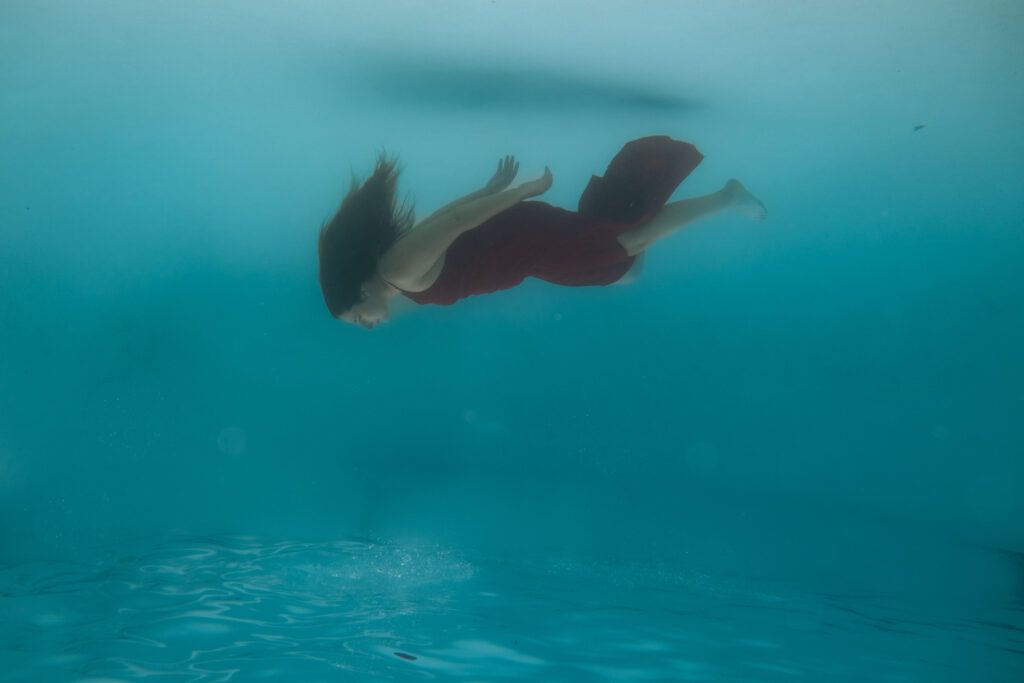 Toujours disponible pour les autres : quand la relation devient à sens unique 3 Femme en robe rouge nageant seule sous l’eau, symbole du retour à soi lorsque l’on est toujours disponible pour les autres.